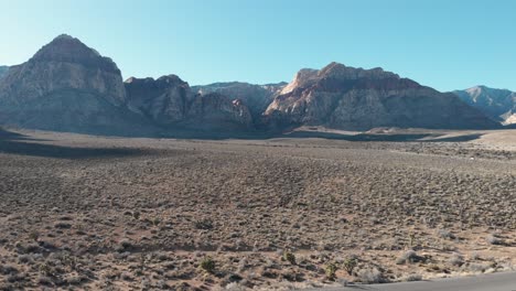 Aerial-drone-shot-of-Red-Rock-Scenic-Highway-with-mountains-in-the-background