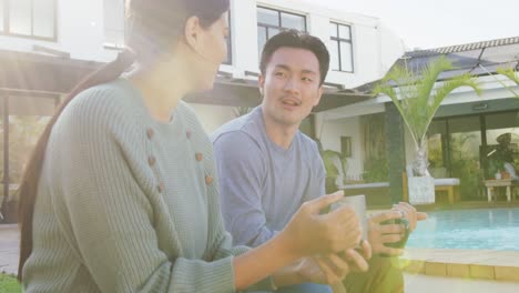 Video-of-happy-diverse-couple-talking-and-drinking-coffee-in-garden