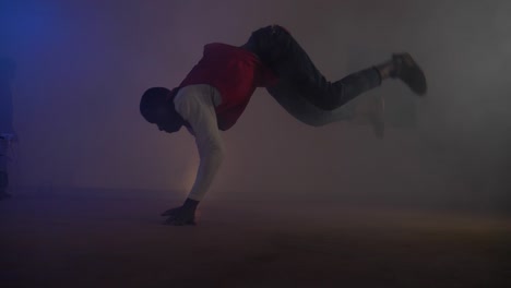 Slow-motion-shot-of-African-youth-in-red-shirt-doing-a-break-dancing-move-jumping-from-his-hands-to-feet-in-colorful-disco-lights-and-smoke