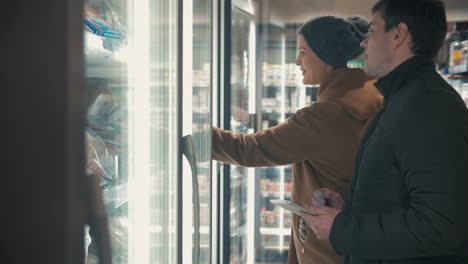 young couple taking frozen food from fridge in the shop