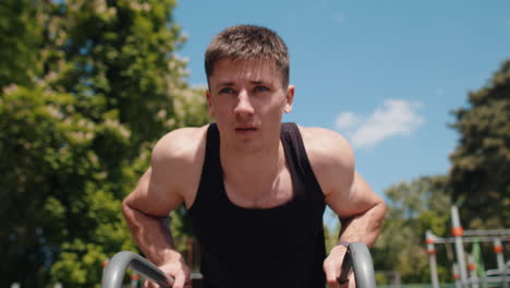 athletic bodybuilder muscular man doing sport workout pushup exercise on parallel bars outdoors