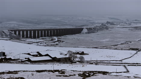 establishing aerial drone shot of ribblehead viaduct and farm on snowy day in yorkshire dales uk