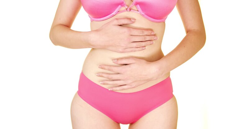Woman in pink bra and underwear grabbing and holding stomach on a seamless white studio backdrop