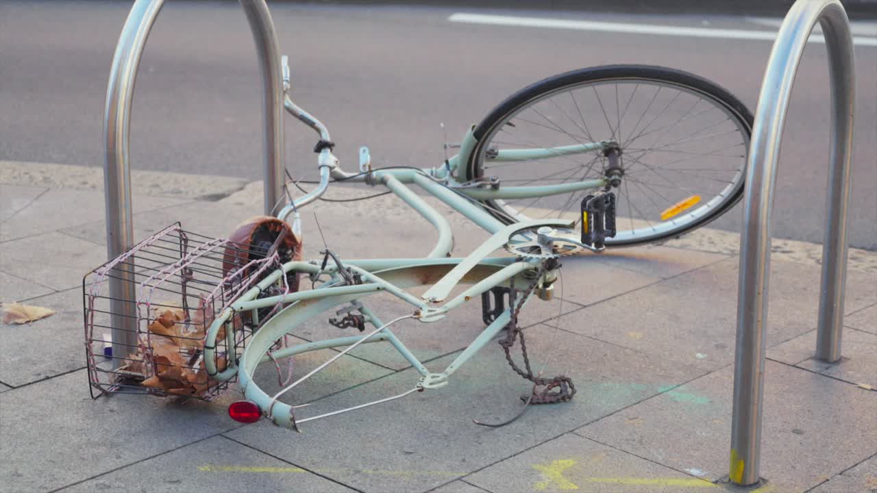 歩道に倒れた自転車が、街路の脇にある金属製の自転車ラックにロックされている手持ち撮影。