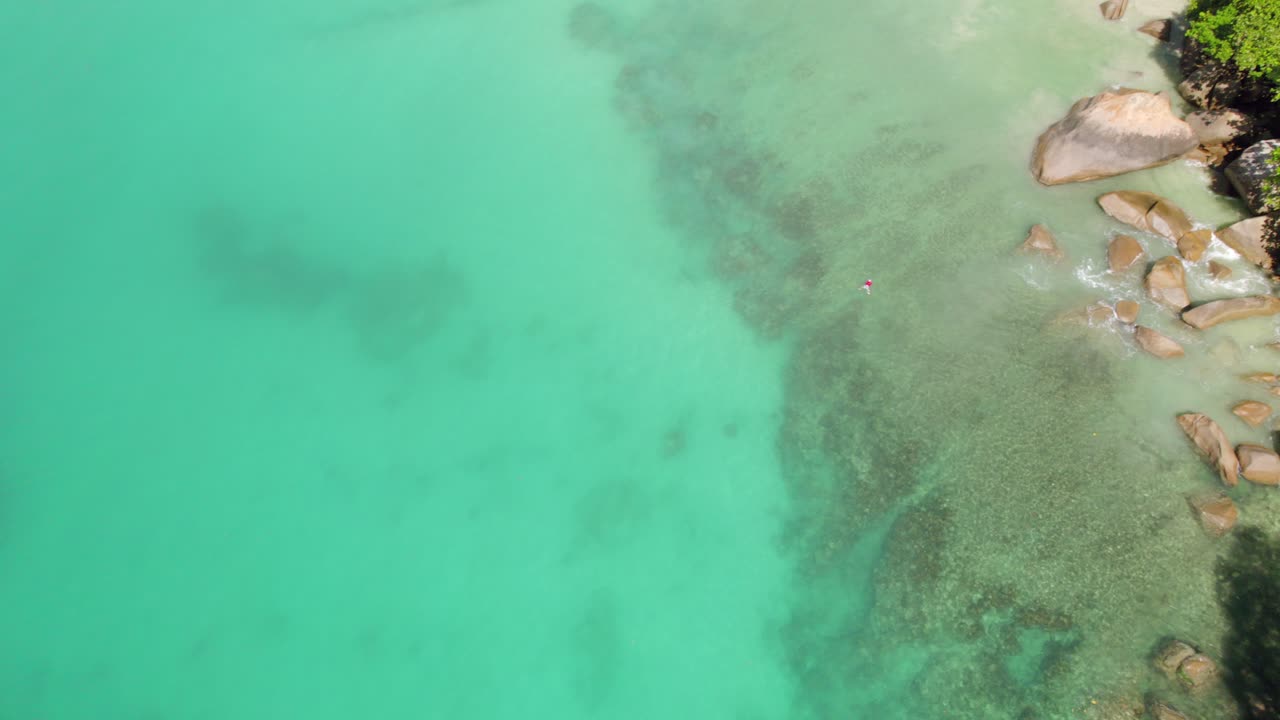 은 셔츠를 입은 남자가 그라나이트 돌, 푸른 물, 앤스 루이스, 마헤 세이스 근처를 지나 돌아 헤엄치는 드론 영상.