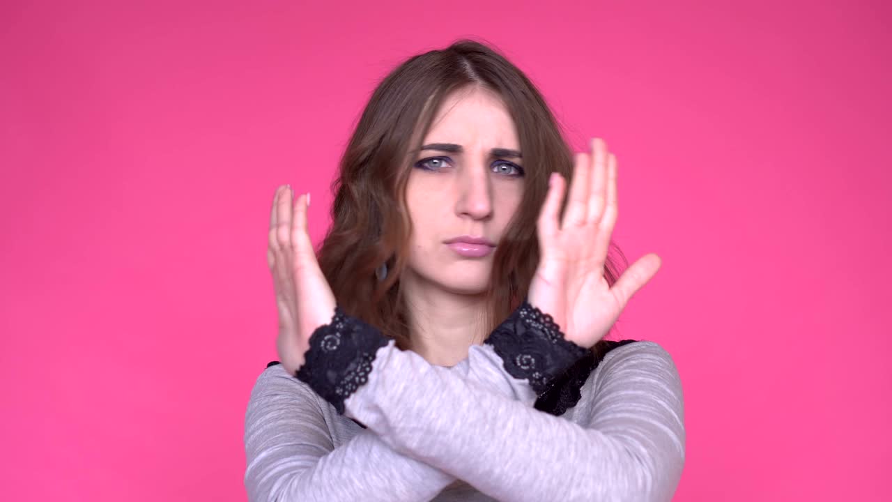 Young woman showing a stop arms crossed while looking at the camera over pink background.