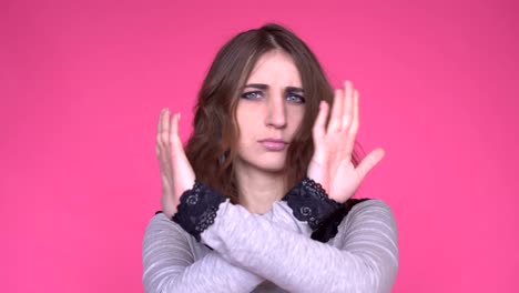 young woman showing a stop arms crossed while looking at the camera over pink background.