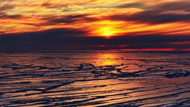 Ice formation on a sea surface under a dramatic sunset sky, reflecting golden light and cold tones