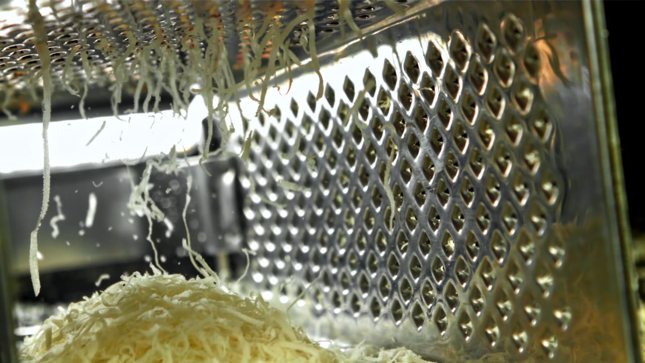 Formaggio grattugiato che cade al rallentatore da una grattugia di metallo