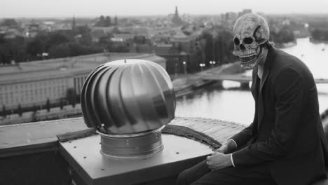 man in skull mask sits on rooftop overlooking city