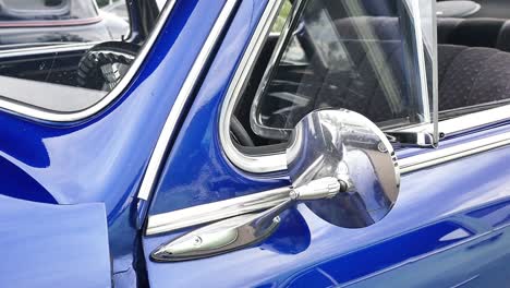 Slow-push-in-on-reflective-side-view-mirror-on-a-blue-classic-car-with-the-windows-down