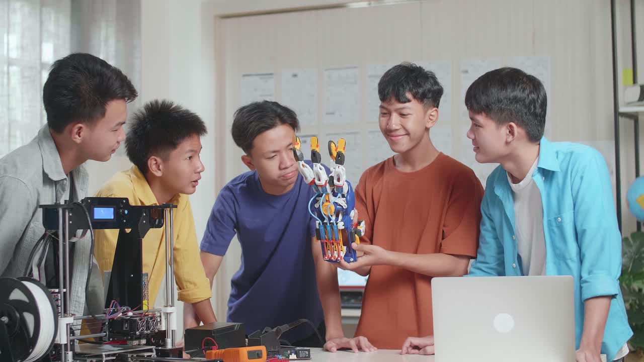 노트북과 3d 프린팅을 가진 젊은 아시아 소년 그룹이 사이보그 손을 확인하고 집에서 일하면서 웃고 있습니다.