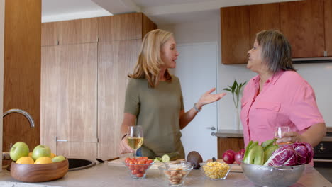 Preparing meal, two multiracial female friends chatting in kitchen with fresh vegetables, at home