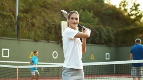 Portrait-Shot-Of-A-Smiling-Woman-Waving-Racket-While-Looking-At-The-Camera-On-A-Tennis-Court