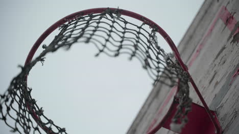 old basketball hoop with torn net hanging in wind and peeled off paint