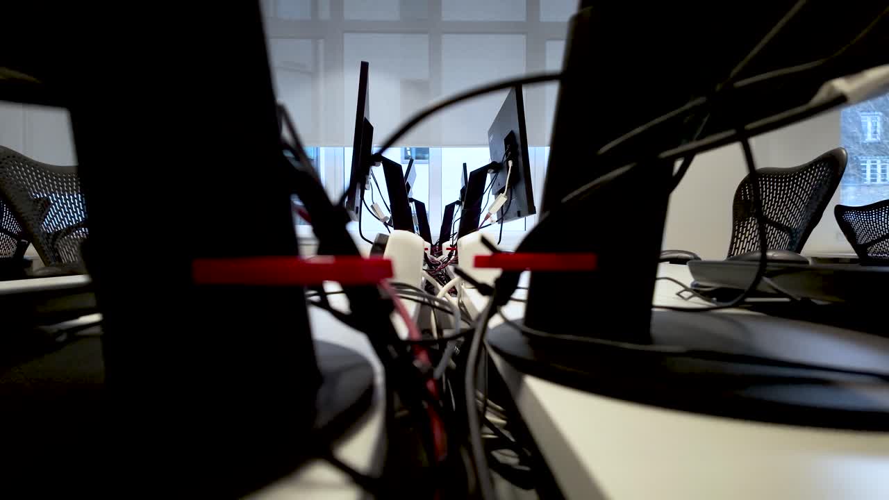 Close up view of tangled wires and cables connecting computer monitors in a modern office, highlighting the complexity of workplace technology