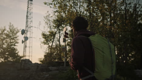 Hiker-walks-up-a-hill-on-rocky-terrain-towards-the-sun,-camera-tracking-from-the-side