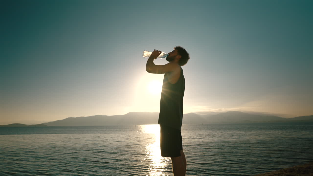 Silhouette of man rehydrating by the ocean at sunrise, wellness and healthy living