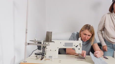 fashion designers adjusting needle on bar tack sewing machine, one helps partner then returns to seat, showing synergy, professional environment, shared skill, efficient production