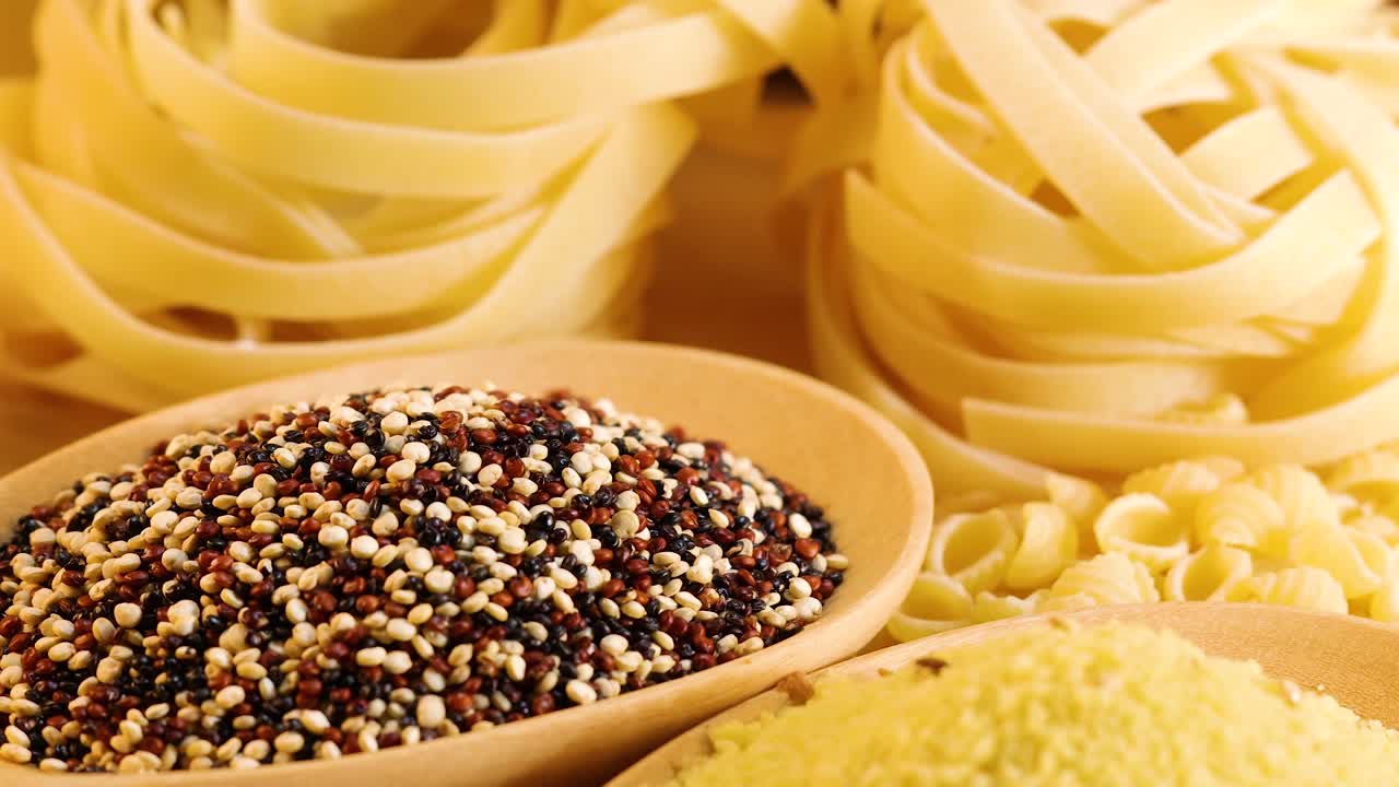 Close-up of various grains and pasta under warm lighting, highlighting textures and colors in a static arrangement
