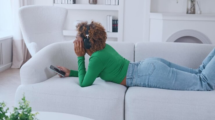 Young beautiful african american woman zoomer lying on sofa listening to music