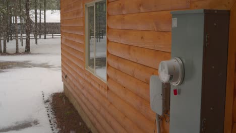 el lado de una cabaña y la caja eléctrica en la nieve