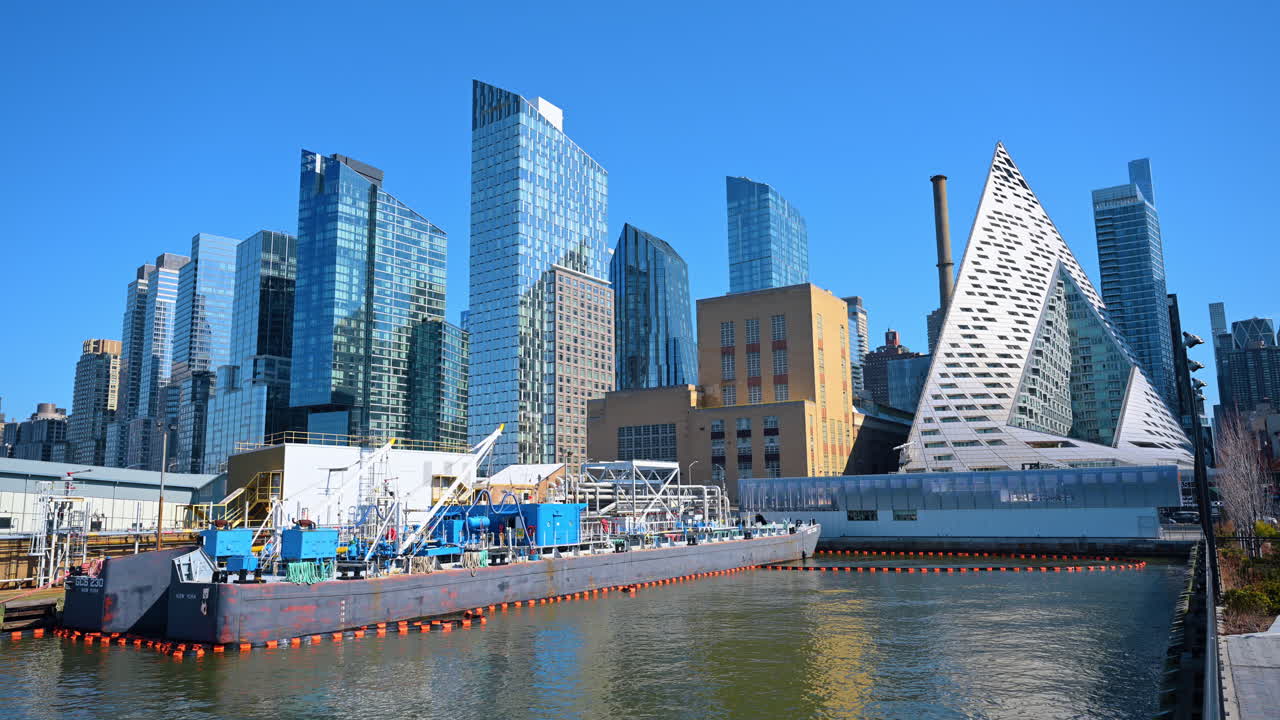 Sà lan công nghiệp neo đậu trên sông Hudson với nền đường chân trời Manhattan. Sà lan công nghiệp lớn trên mặt nước trước kiến trúc hiện đại bao gồm tòa nhà kim tự tháp VIA 57 West ở Thành phố New York.