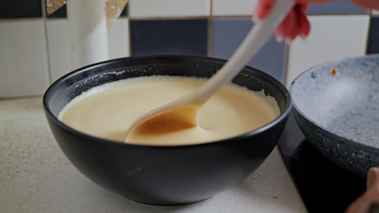 Creamy pancake batter swirls smoothly in slow motion during gentle hand stirring