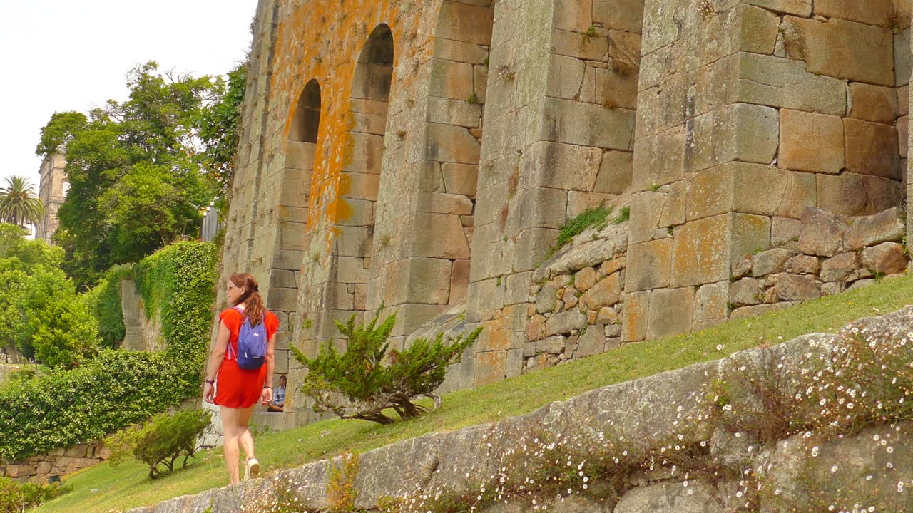 toma de bajo ángulo de una mujer con un vestido naranja apreciando el parque de las virtudes, oporto, portugal en un día nublado