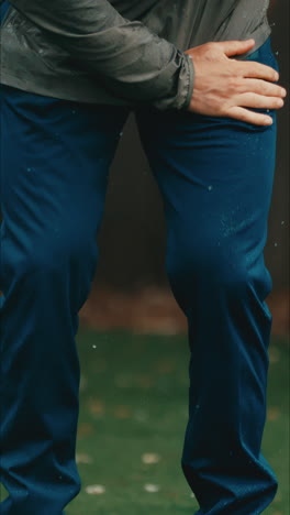 man uses hand to brush water off waterproof blue pants and rain droplets fly everywhere in slow motion