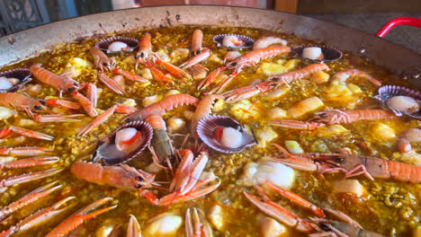 cooking a huge traditional spanish seafood paella dish with shrimps, st jacques scallops and cigala norway lobsters nephrops norvegicus, delicious cooked rice with seafood, marbella spain, 4k shot