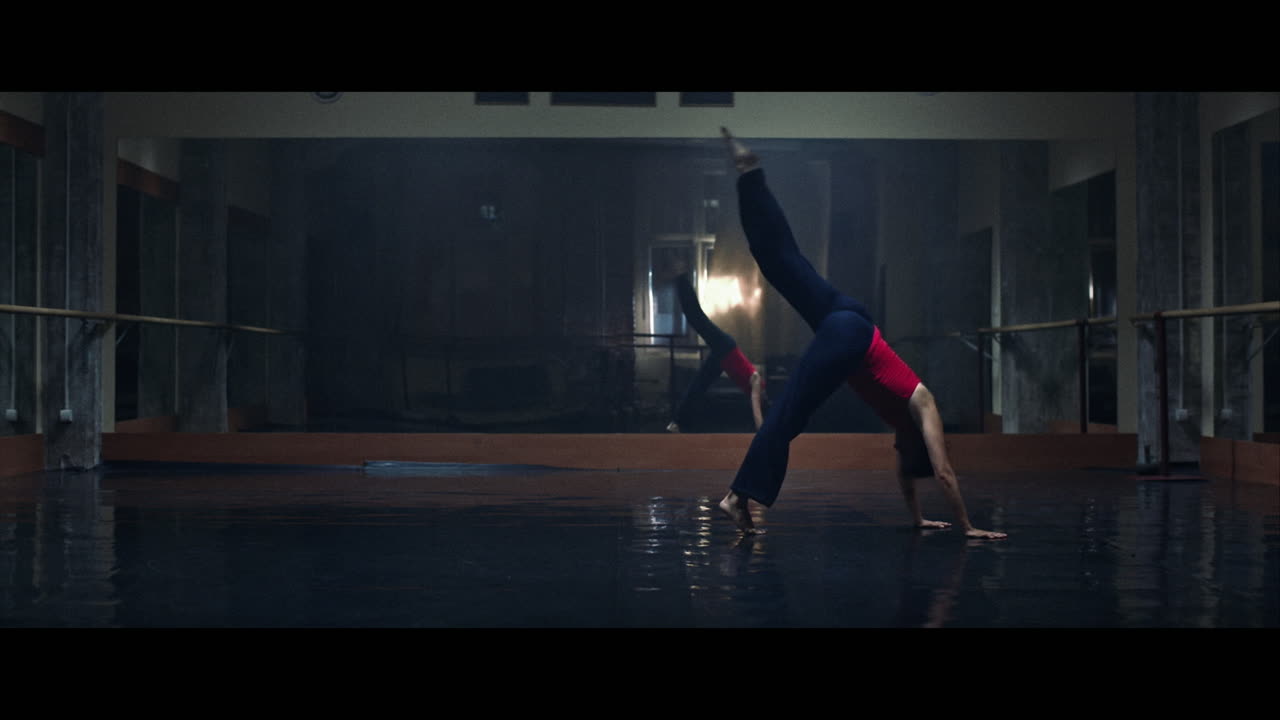 A young woman practices modern dancing and ballet in a moody room full of mirrors