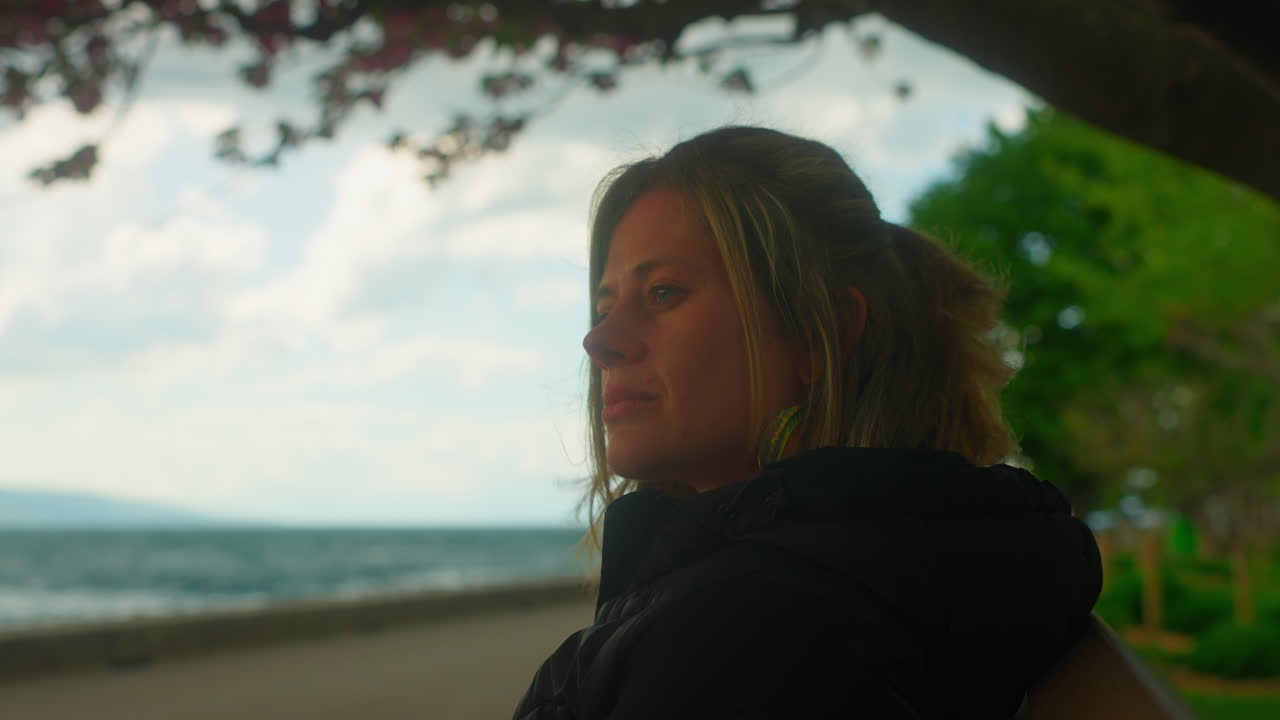 mujer sentada en un banco y mirando la vista en cámara lenta, mientras que los pétalos de la flor del cerezo vuelan en el viento