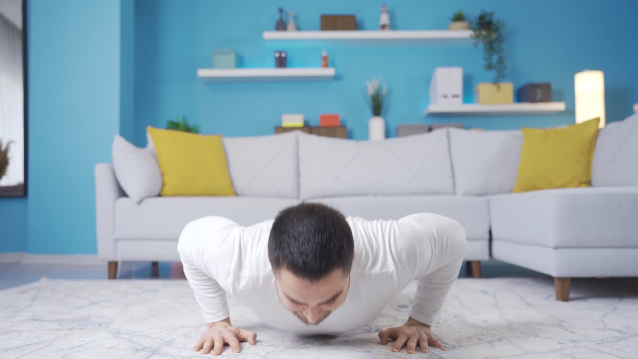 집에서 푸시업을 하는 젊은 남자가 카메라를 쳐다보고, 푸시업을 하는 방법을 보여주는 운동선수 젊은 남자가 있습니다.