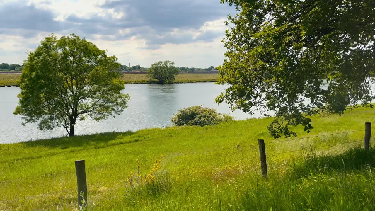 pintoresco río mosa durante la primavera con árboles verdes nubes y una valla