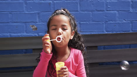 In-school,-a-young-African-American-girl-blows-bubbles,-blue-background