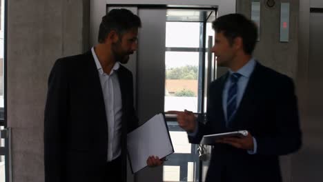 Businessmen-interacting-with-each-other-while-getting-out-of-elevator