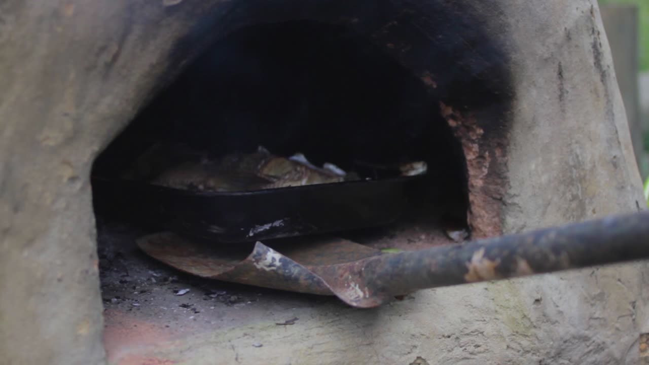 Un pesce in cottura in una padella inserita in un forno a pietra artigianale all'aperto