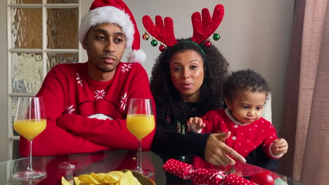 young parents with small child on christmas video call listening and talking to camera