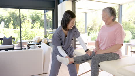physiotherapist assisting senior asian woman with leg exercises at home therapy session
