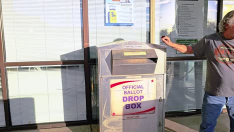 older man votes in election by dropping mail-in ballot letter in slot at voting booth with offical ballot drop box sign for democratic government campaign in presidential race