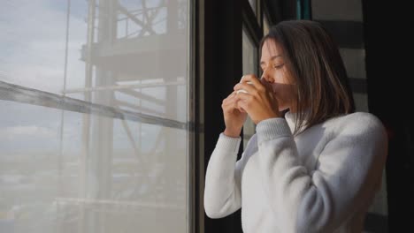 여성 갈색은 넓은 창문 근처에 커피 컵을 마시고, 빛을 즐기고