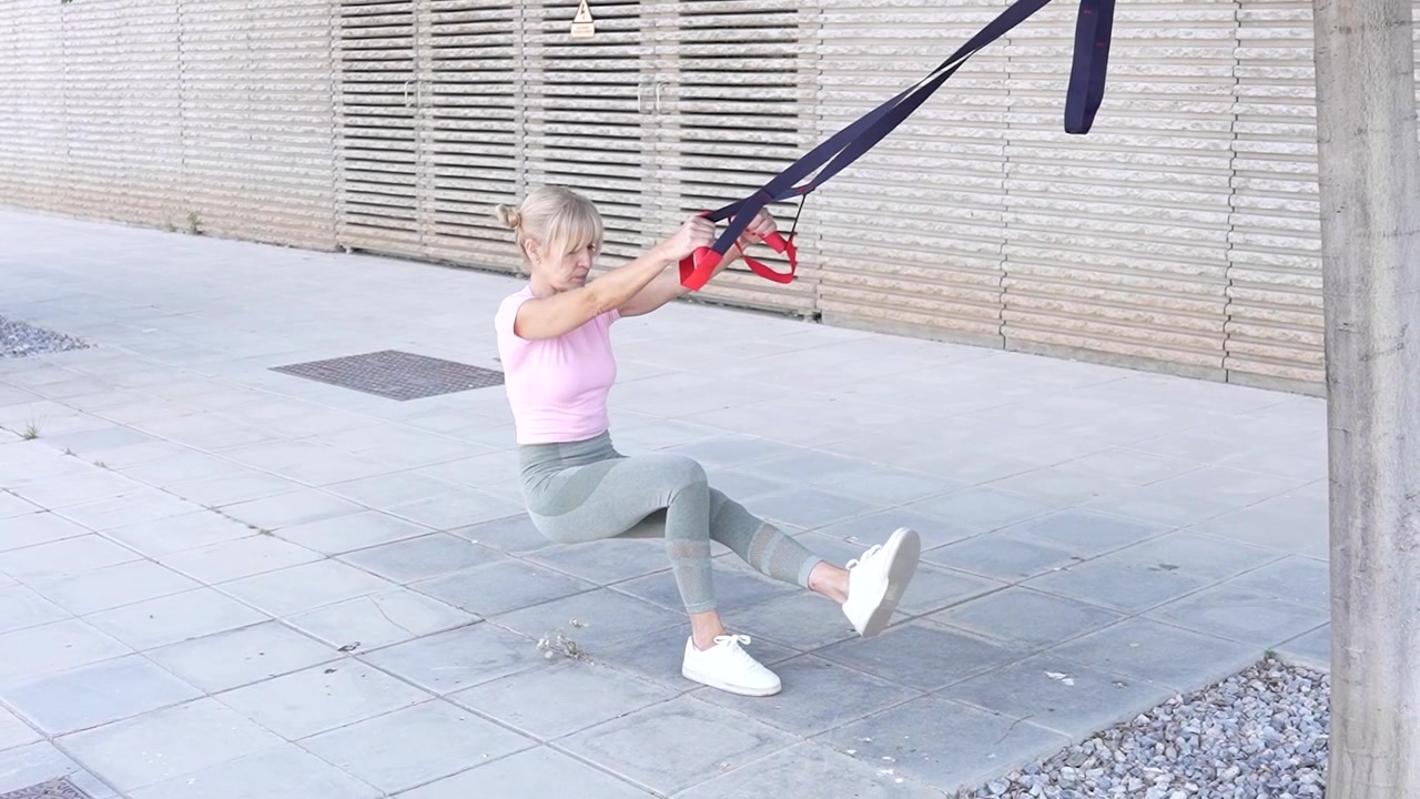 A woman is working out using suspension straps outdoors focusing on athleticism and strength
