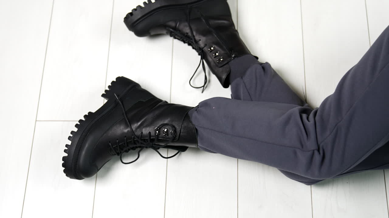 Presentation of black leather stylish army boots with laces. Modern sitting on the floor showing her modern footwear on tractor soles.