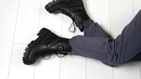 presentation of black leather stylish army boots with laces. modern sitting on the floor showing her modern footwear on tractor soles.