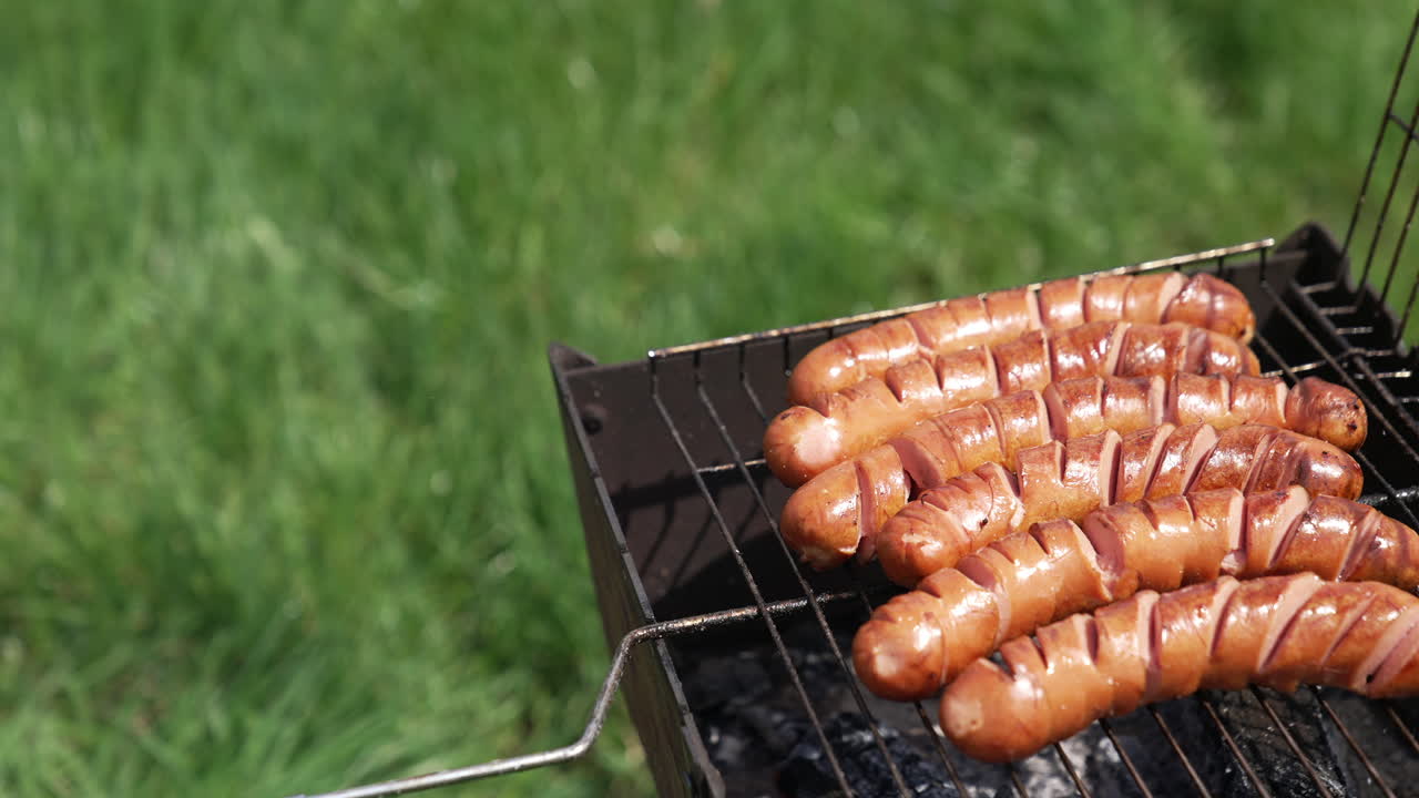 Sausages on grill. Cooking hot dog sausages on a grill grate in nature. Grilling food during the summer vacation. Barbecue outdoors.