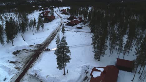 Vuelo-Aéreo-A-La-Izquierda-Sobre-Un-Paisaje-Nevado-De-Fulufjallsbyn-En-Suecia-Con-Una-Moto-De-Nieve-Girando-La-Carretera-En-Una-Carretera-Rural-Que-Conduce-A-Un-Bosque