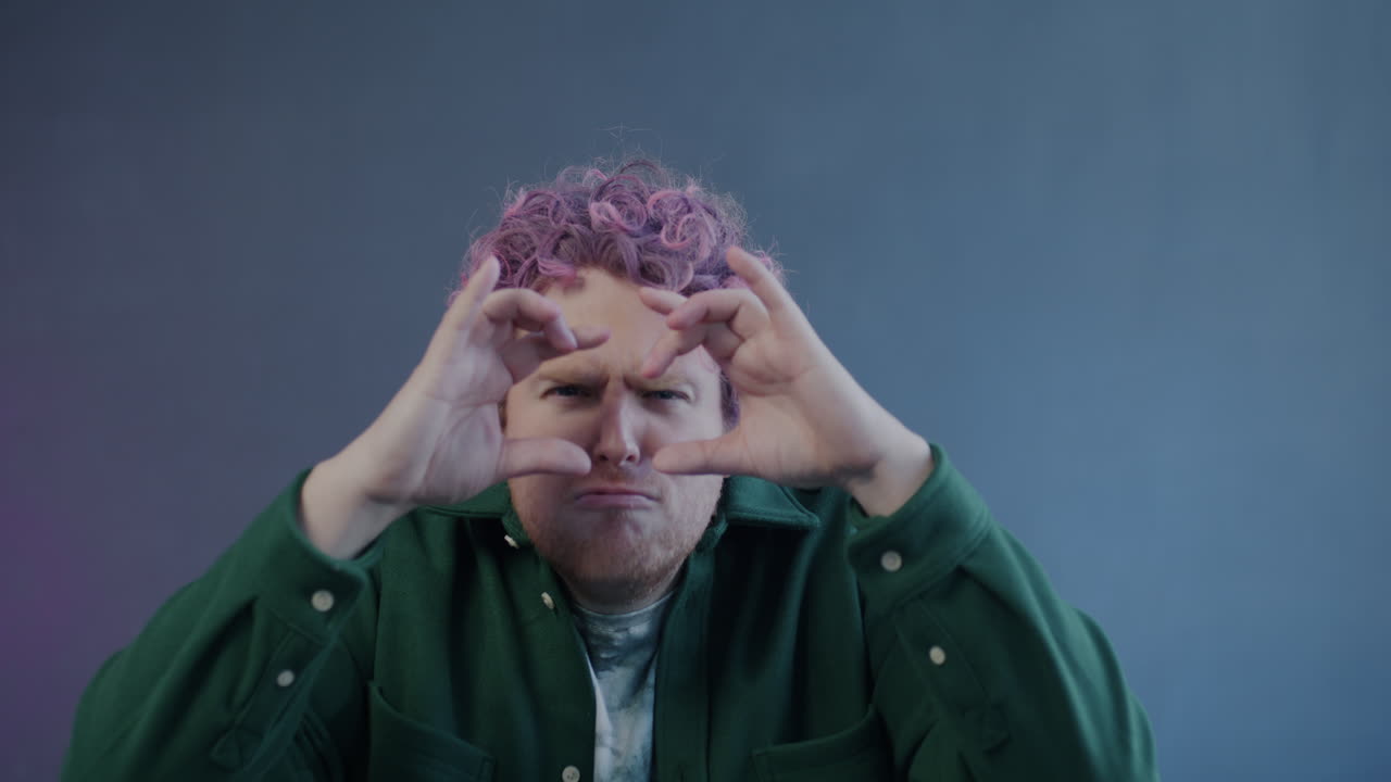 Man with pink hair making a heart shape with hands