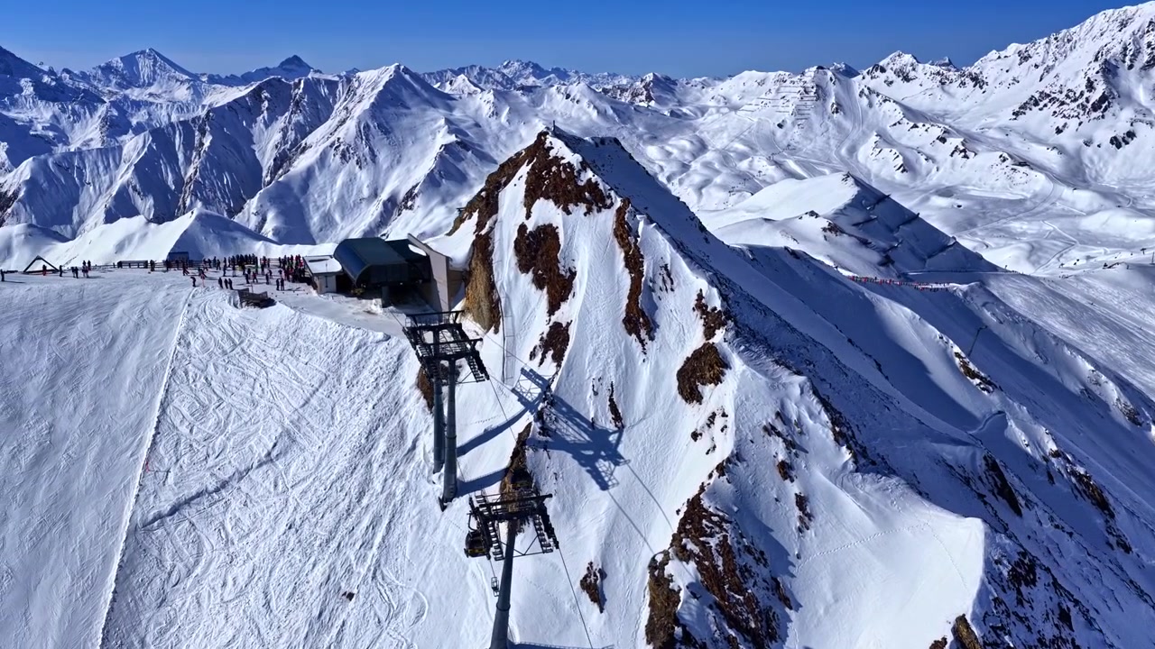 Montagna innevata con stazione di risalita e cime frastagliate.