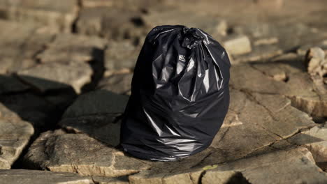 black trash bag lay on a rocky beach